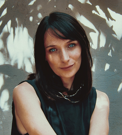 A cinematic portrait of Eugenia Brodsky against a wall with dappled leaf shadows and warm, natural lighting.