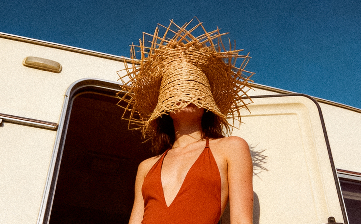 Flux AI generated cinematic fashion story shot from a low angle featuring a model in a rust-orange swimsuit and a large structural straw hat standing in a camper van doorway, realistic film style by Leonardo Losito for VGXW Magazine via Virtuogenix.Online